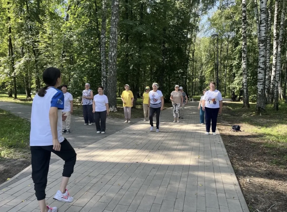 Участники зеленого фитнеса выполняют групповое упражнение на аллее Парка Победы